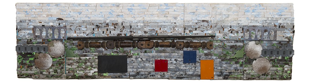 Abstract mixed-media sculpture featuring metallic, wooden, and textured elements arranged against a layered blue-gray background with pops of red, black, blue, and orange.