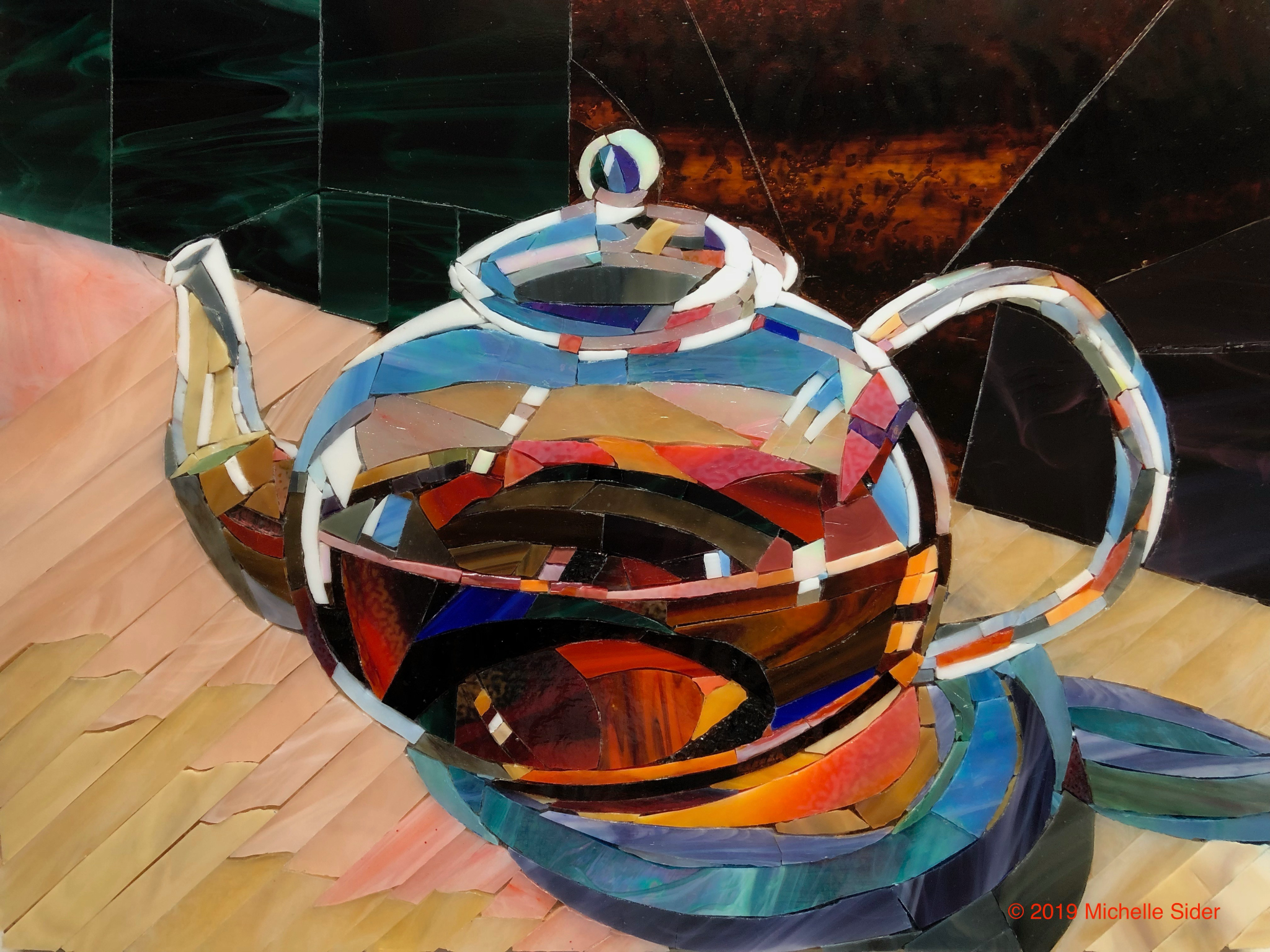 Glass mosaic still life of a multicolored teapot filled with dark tea on a light wooden surface, with a blue saucer-like shape to the right and a dark green-and-brown background.