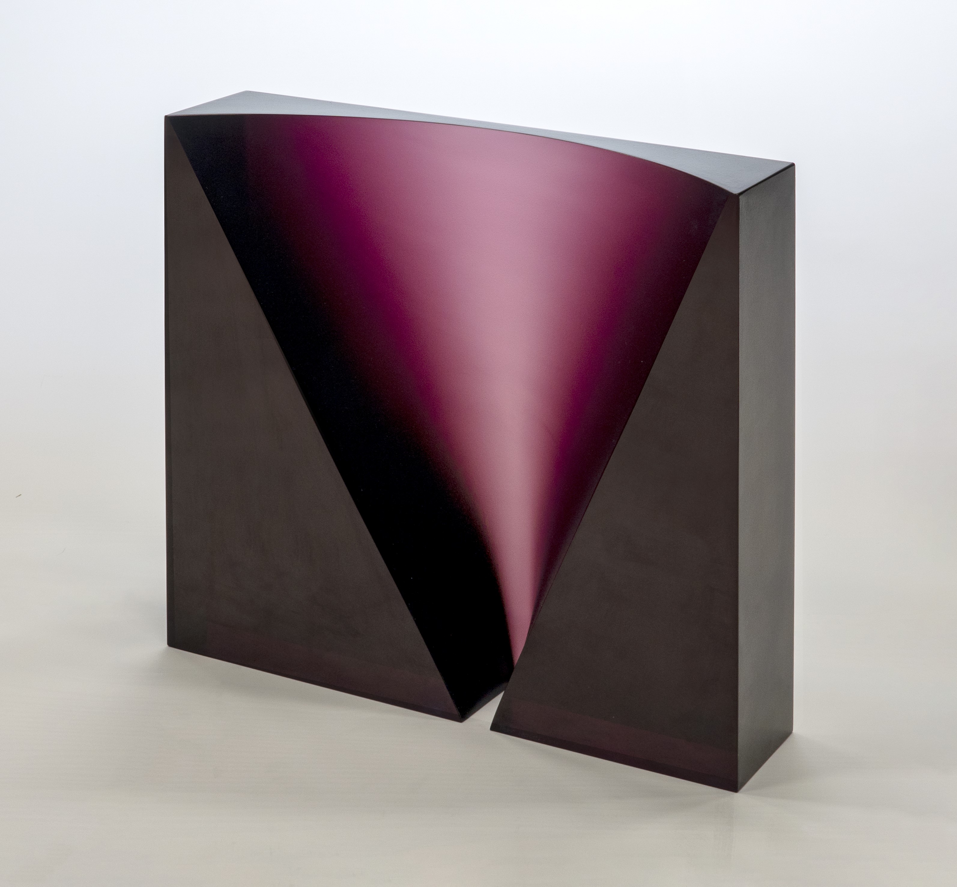 A modern, geometric glass sculpture with a rectangular form and a triangular cutout in the center. The cutout reveals a smooth, concave surface in a rich, reflective purple color, contrasted by the sculpture’s matte black exterior.