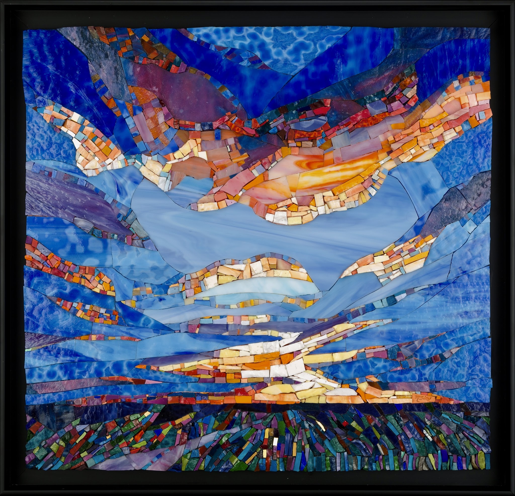 Framed abstract glass mosaic of a seascape with layered blue waves and sky, streaks of orange and red suggesting a glowing sunset, and a band of multicolored tiles along the bottom like shoreline or vegetation.